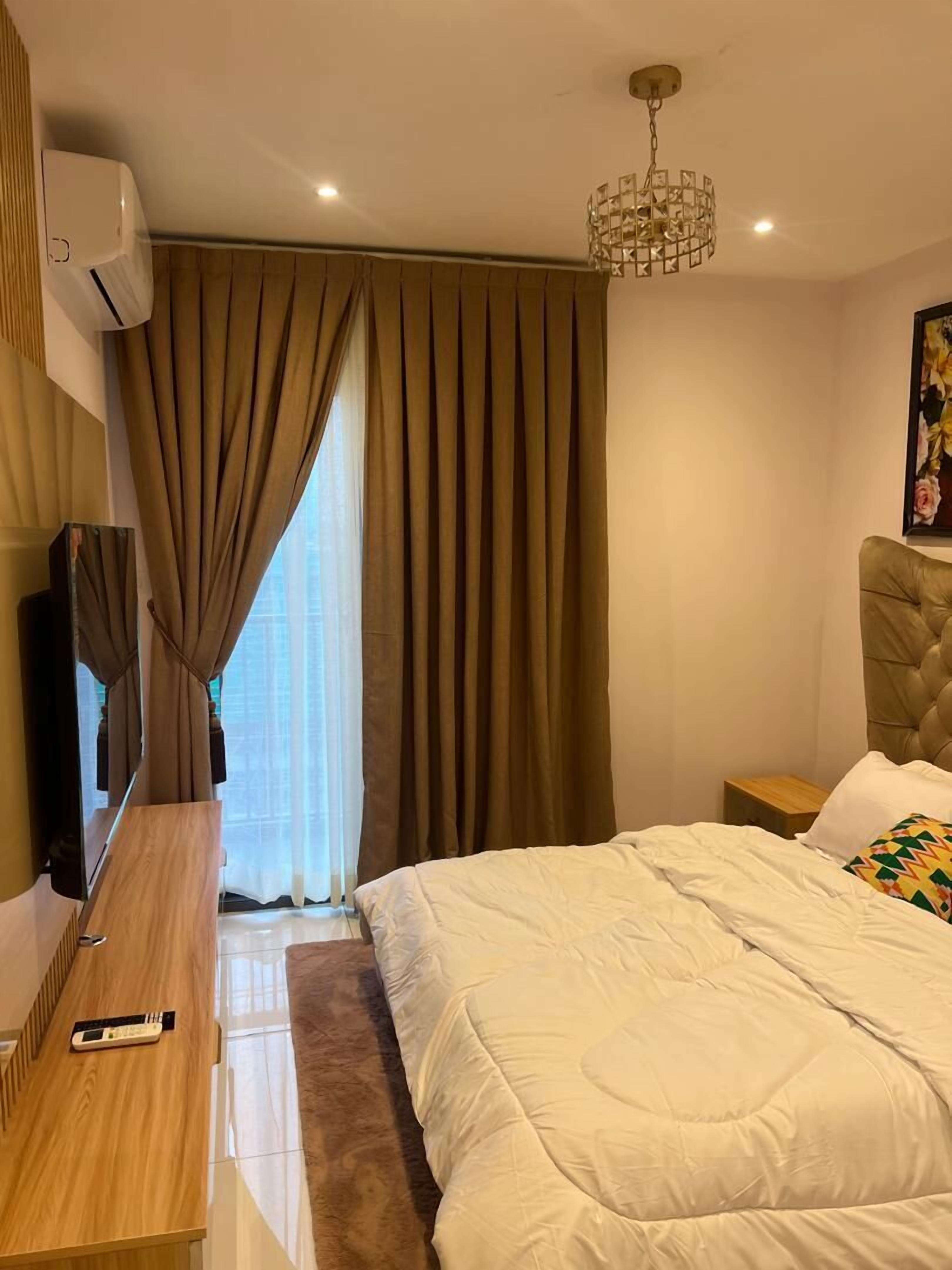 A modern hotel room with a bed, a wooden desk, a television, and a chandelier.