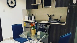 Moderni keittiö, jossa on lasinen ruokapöytä, kaksi sinistä tuolia, mikroaaltouuni, liesi ja pesukone.