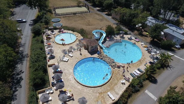 Luchtbeeld van een resort met twee grote zwembaden, ligbedden, parasols en een kleine glijbaan.