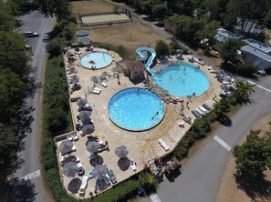 An aerial view of a resort with two large swimming pools, sun loungers, umbrellas, and a small water slide. - Camping Le Clou - Lodge de Luxe (Coux-et-Bigaroque)