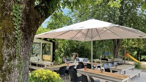 Een terras met tafels en stoelen, omgeven door bomen en een speeltuin.