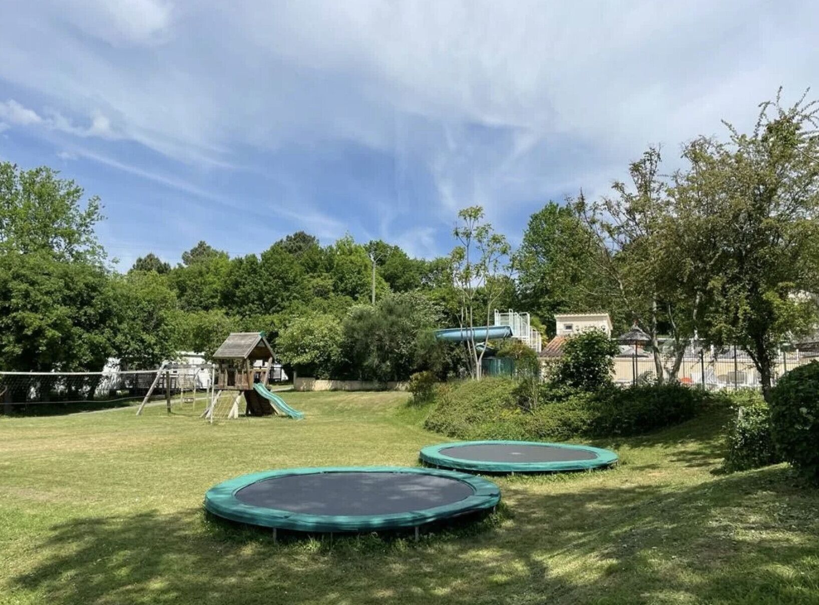 Un patio de juegos con dos trampolines, un tobogán y una pequeña estructura de madera.