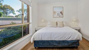 A bedroom with a bed, two bedside tables, a ceiling fan, a window with a view of greenery, and a framed picture on the wall. - Pete's Retreat - Coastal Comfort Just Steps from t (Noraville)