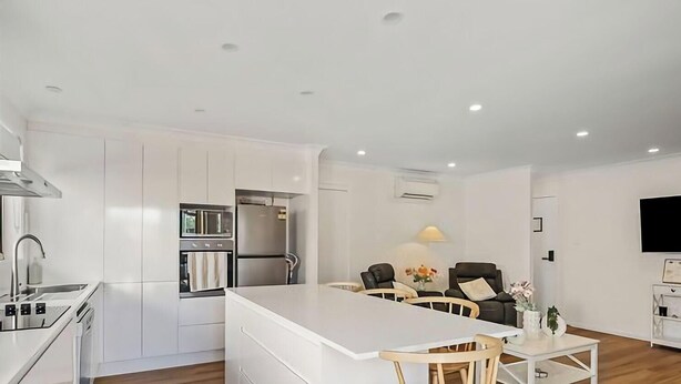 A modern kitchen with white cabinetry, a stainless steel range hood, and a central island with seating. - Pete's Retreat - Coastal Comfort Just Steps from t (Noraville)