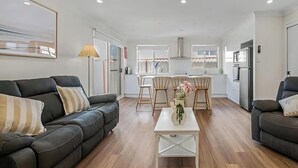 A modern living room with a sofa, coffee table, and a dining area with chairs. - Pete's Retreat - Coastal Comfort Just Steps from t (Noraville)