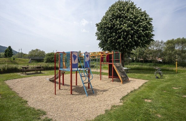 Ein Spielplatz mit Rutsche, Klettergerüsten und einem Picknicktisch auf einer Rasenfläche.