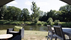 An outdoor seating area with wicker furniture and a view of a river and trees. - Camping Gritt - De Lodge (Erpeldange-sur-Sûre)