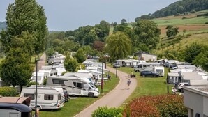 A caravan park with multiple caravans parked on a paved area, surrounded by greenery and hills in the background. - Camping Gritt - De Lodge (Erpeldange-sur-Sûre)