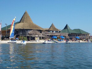 Ein Strandresort mit strohgedeckten Gebäuden, einer Pier und Liegestühlen.