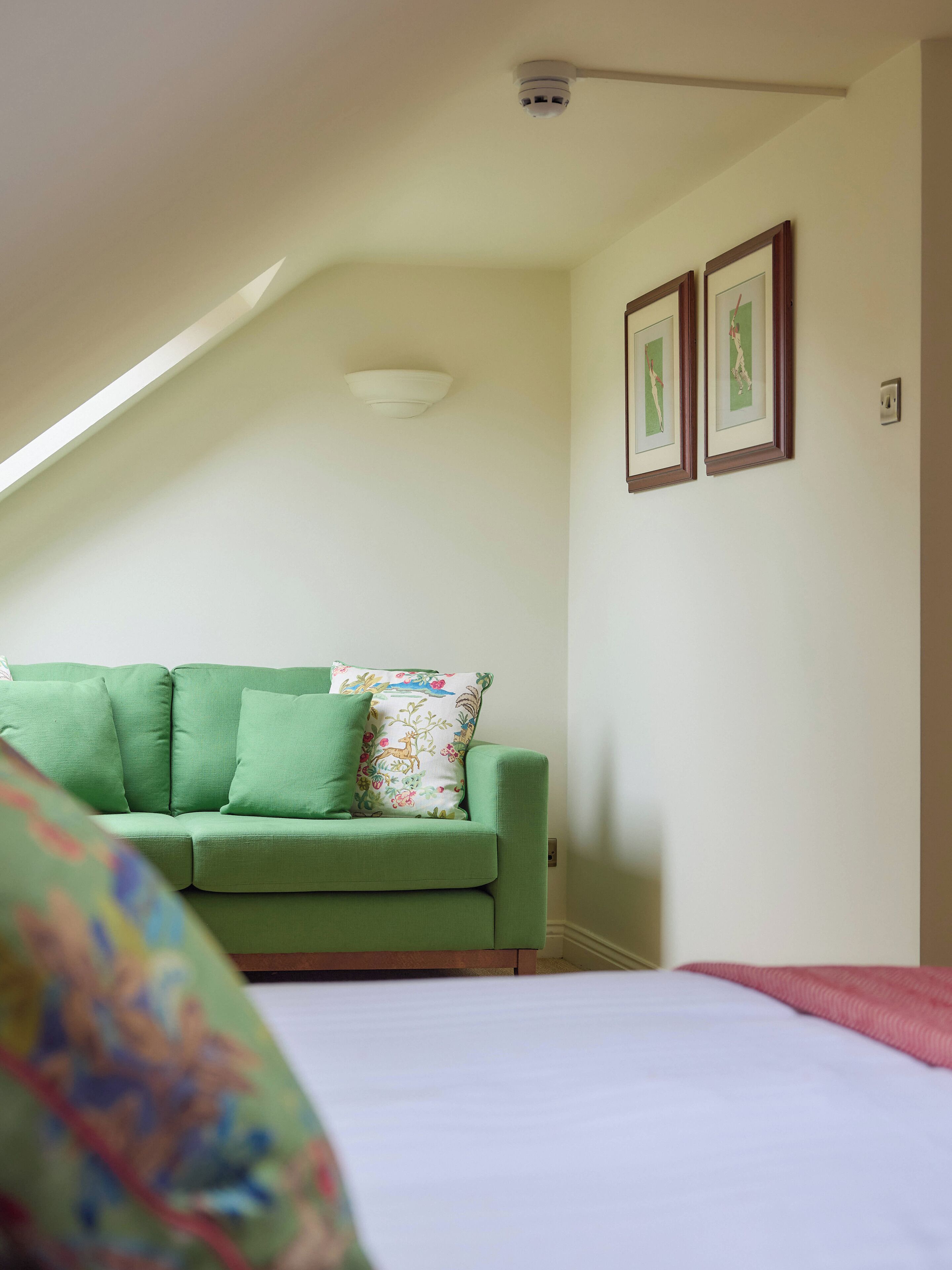 Una habitación con un sofá verde, una cama blanca y dos cuadros en la pared.