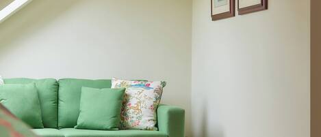 Una habitación con un sofá verde, una cama blanca y dos cuadros en la pared.