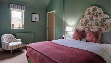 Un dormitorio con una cama, una silla, un radiador, una puerta, una ventana y una pared con un cuadro enmarcado.