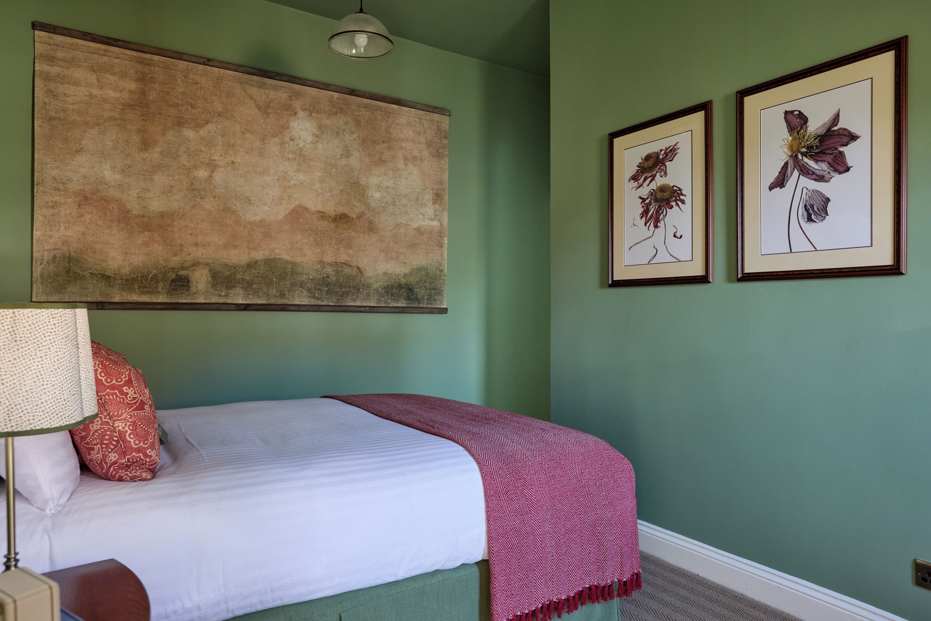A bedroom with a bed, a large abstract painting, and two framed floral artworks on the wall.
