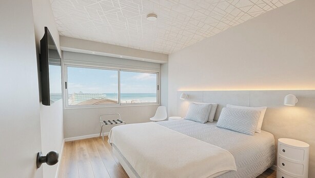 A bedroom with a large bed, a window with a view of the beach, a chair, and a bedside table. - Design apartment in historic district with river view (Montevideo)