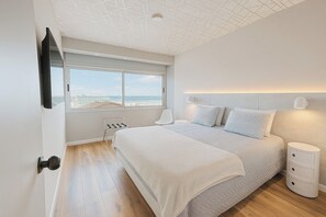 Una camera da letto con un letto grande, una finestra vista spiaggia, una sedia e un comodino.