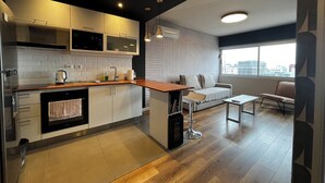 A modern kitchen with white cabinets, a wooden countertop, and a built-in oven. There is a dining area with a white sofa and a small table. - Design apartment in historic district with river view (Montevideo)