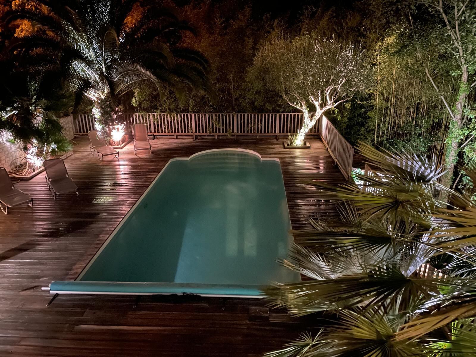 A swimming pool with a wooden deck, surrounded by trees and a wooden fence.