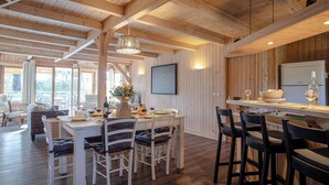 A spacious dining area with a wooden ceiling and a large window. There is a dining table with chairs and a bar counter with stools. - Charming all-wood villa with heated pool -4 bedrooms -3 bathrooms (Biscarrosse)