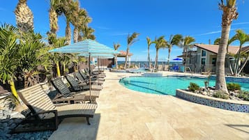 A poolside area with lounge chairs and umbrellas, a clear blue sky, and a view of the ocean.