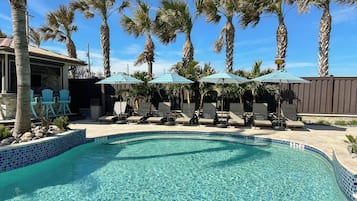 A swimming pool with lounge chairs and umbrellas, surrounded by palm trees.