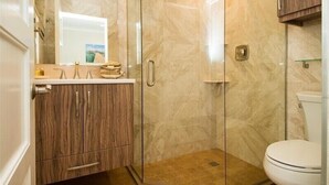 A bathroom with a glass-enclosed shower, a white toilet, and wooden cabinets. - The Rod and Reel Resort-Suite 5 (Anna Maria)