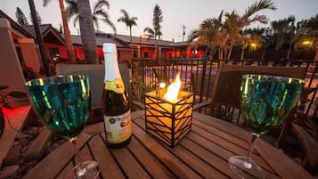 Ein Holztisch mit zwei grünen Gläsern, einer Martini-Flasche und einer brennenden Kerze in einem quadratischen Laternengefäß.