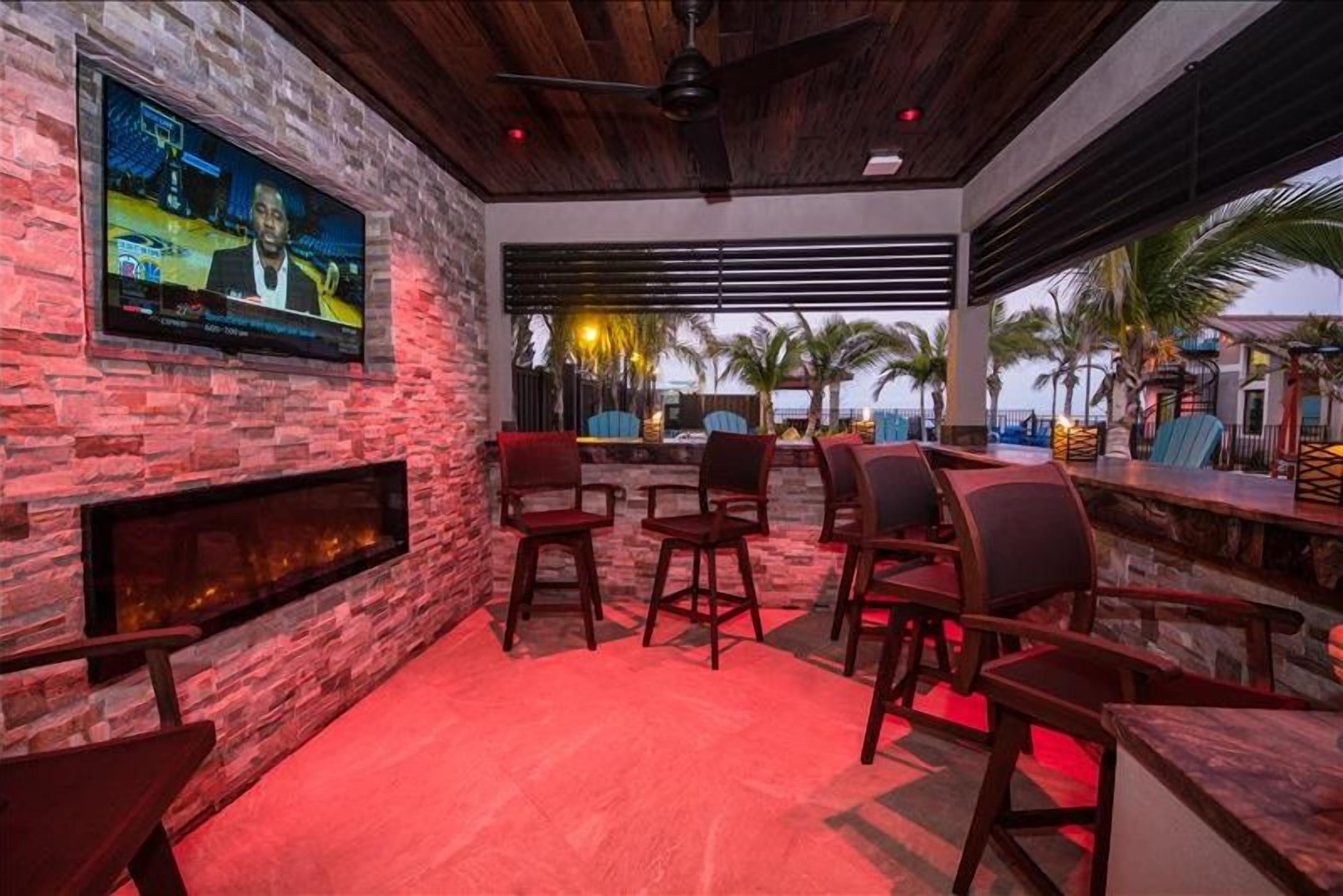 A bar area with stone walls, a flat-screen TV, and outdoor seating with palm trees.