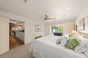 Ein Schlafzimmer mit einem großen Bett, einem Deckenventilator und Blick auf den Garten durch eine Schiebetür.