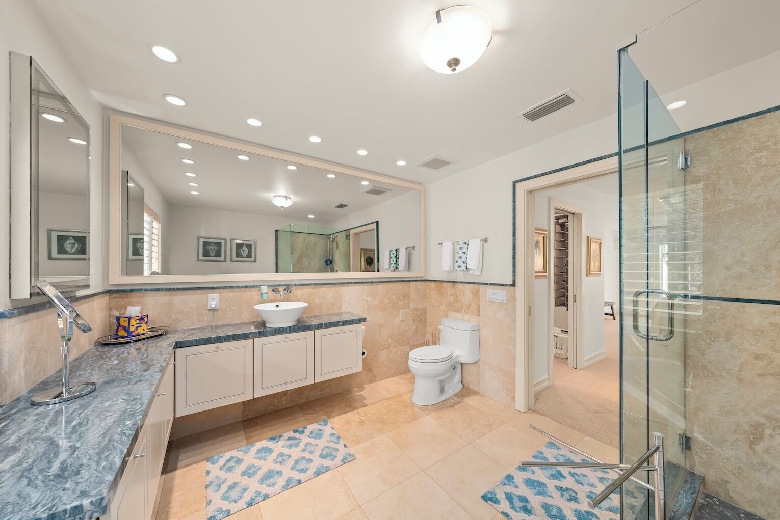 A modern bathroom with a large mirror, a sink, a toilet, and a shower area.