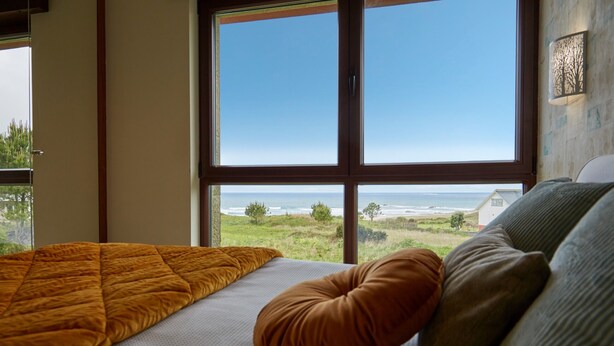 Un dormitorio con un ventanal grande, una cama con colcha y vistas a la playa.