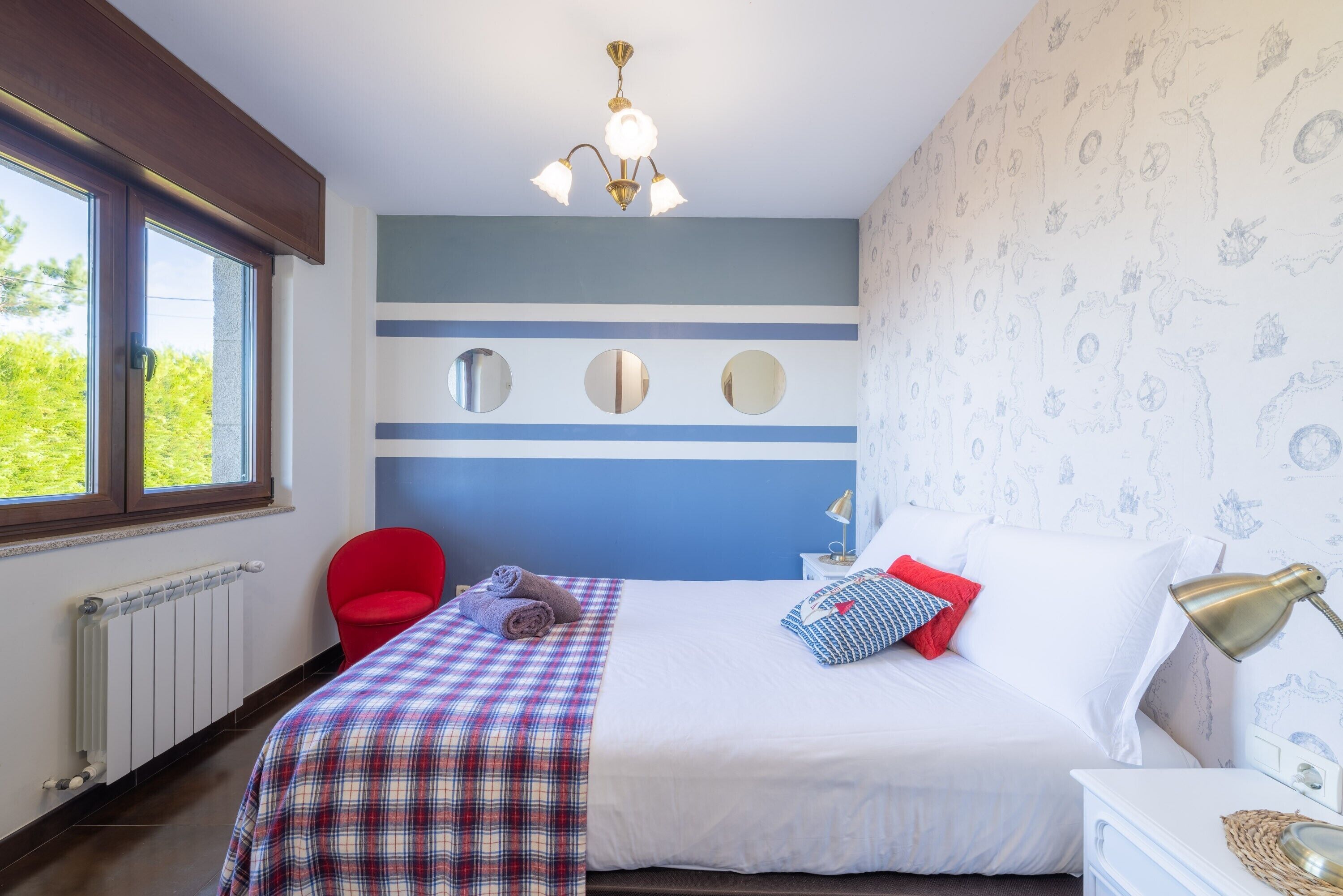 Een slaapkamer met een bed, een rode stoel, een raam, een radiator en een kroonluchter.