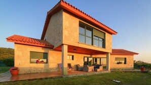 Una casa moderna de dos pisos con techo plano, ventanas amplias y un área de estar al aire libre techada.