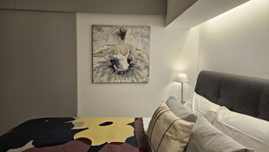 Hotellihuone, jossa on sänky, taulu seinällä ja yöpöytälamppu.
