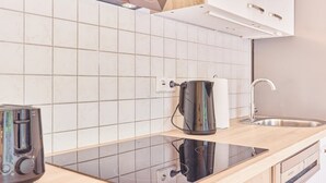 A modern kitchen with a black induction cooktop, a stainless steel kettle, and a sink with a modern faucet. - Lena Your break (Buchen)