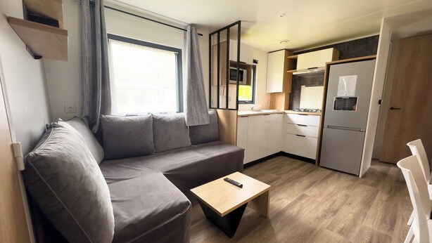A compact living space with a sofa, a small table, a kitchenette, and a door leading to another room. - Domaine Des Acacias Tours (La Ville-aux-Dames)