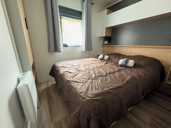 Une chambre à coucher avec un lit, une fenêtre avec des rideaux, un radiateur et une tête de lit.