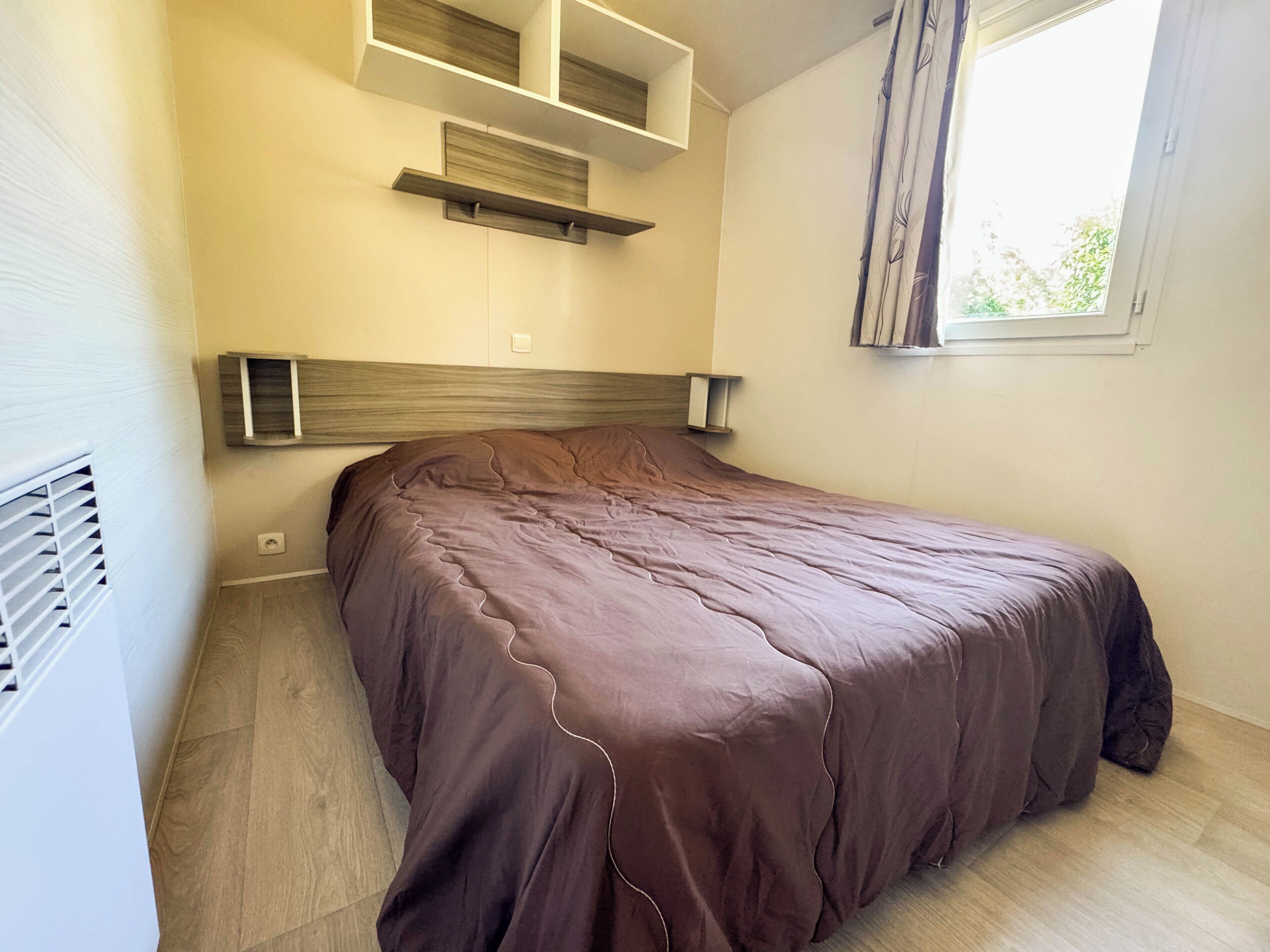 A bedroom with a bed, built-in shelving, a window, and a radiator.