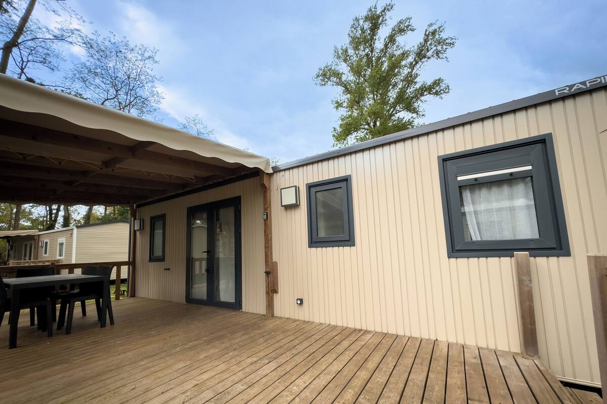 A wooden deck with a covered seating area and a small building with windows.