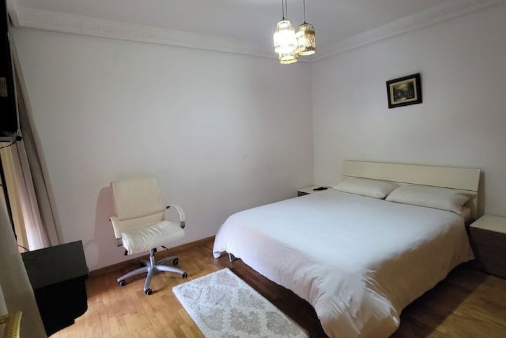Quarto com cama, uma cadeira, tapete e luminária no teto.