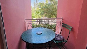 Ein kleiner Balkon mit rundem Tisch und Stuhl, einem Metallgeländer und Blick auf Bäume und Grün.