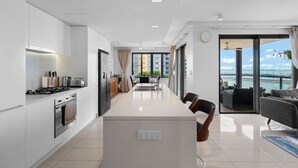 A modern kitchen with a central island, a dining area with a view, and a balcony with a view. - Zen Paradiso Harbour View Pool Balcony (Darwin)