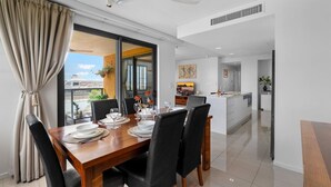 A modern dining area with a wooden table set for four, black chairs, and a view of a cityscape through large windows. - Zen Paradiso Harbour View Pool Balcony (Darwin)