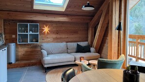 Ein gemütliches Blockhaus-Interieur mit Holzbalkendecke, Dachfenster, einer Couch, einem Esstisch und einer Stern-Dekoration an der Wand.