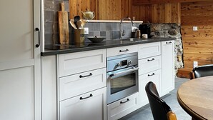 Eine Küche mit weißen Schränken, einer Steinrückwand, Holzbalken, einer Steinarbeitsplatte und einem runden Holztisch.