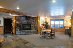 A spacious room with a stone fireplace, wooden furniture, and large windows. - Black Bear Cabin, shared hot tub, walk to slopes! (Crested Butte)
