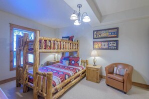 A rustic bedroom with a wooden bunk bed, a small wooden nightstand, a chair, and a ceiling light fixture. - Black Bear Cabin, shared hot tub, walk to slopes! (Crested Butte)