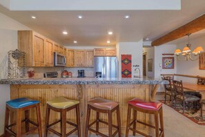 A kitchen with wooden cabinets, a granite countertop, and a bar area with stools. - Black Bear Cabin, shared hot tub, walk to slopes! (Crested Butte)