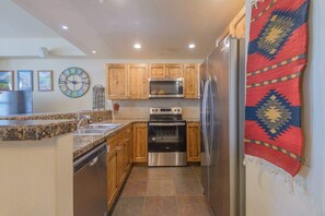 A kitchen with wooden cabinets, stainless steel appliances, a granite countertop, and a patterned rug. - Black Bear Cabin, shared hot tub, walk to slopes! (Crested Butte)