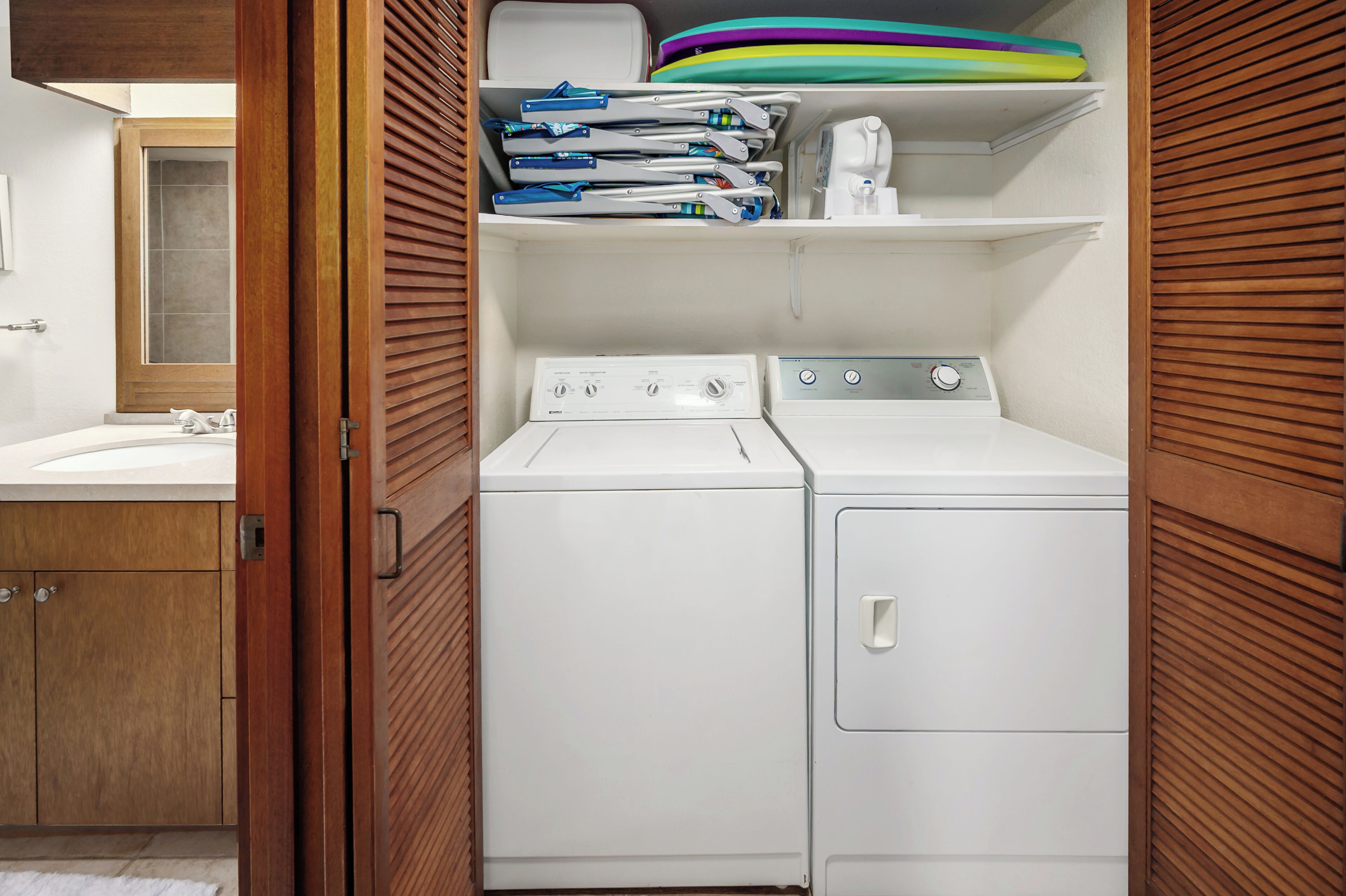 Un cuarto de lavandería con lavadora, secadora y estantes con ropa doblada y productos de limpieza.