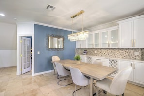 A dining area with a wooden table and four chairs, a chandelier, and white cabinets. - 5700 sqft Lux Golf Villa w Pool & Spa Near Strip (Henderson)